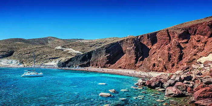 Caldera Beach in Santorini, Greece showing volcanic cliffs, dark pebbles, and deep blue Aegean Sea water