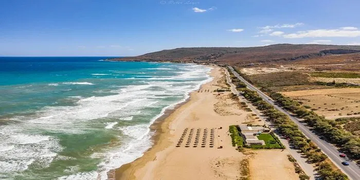 Episkopi Beach in Crete, Greece, showing a long sandy shoreline with calm turquoise waters and mountains in the background