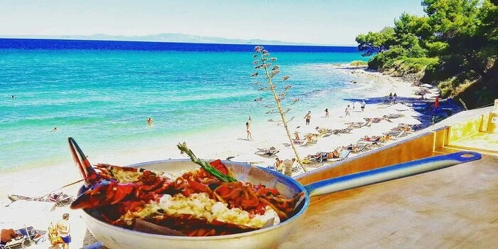 Kriopigi Beach in Halkidiki, Greece with clear blue water and pine trees along the shoreline