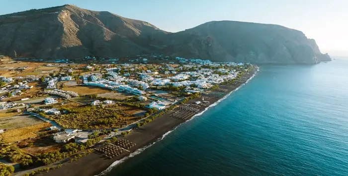 Perissa Beach Santorini with black volcanic sand, clear blue water, and Mesa Vouno mountain in the background
